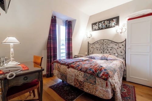 Classic hotel room at Hôtel des Bains with ornate bed, desk lamp, purple curtains, and city view from window