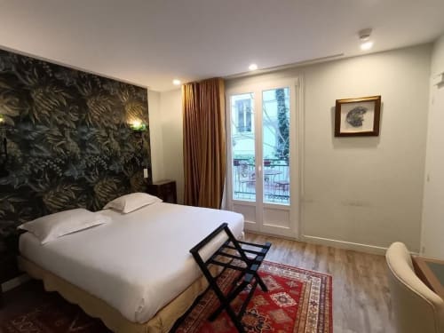 Chambre moderne à l'Hôtel des Bains avec vue sur le jardin, lit blanc, tête de lit botaniste foncée et portes-fenêtres