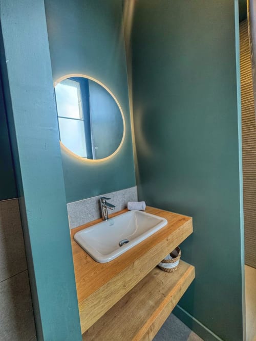 Élégant meuble-lavabo blanc avec vasque en céramique, plan de travail en bois et miroir rond rétroéclairé à l'hôtel O LIT