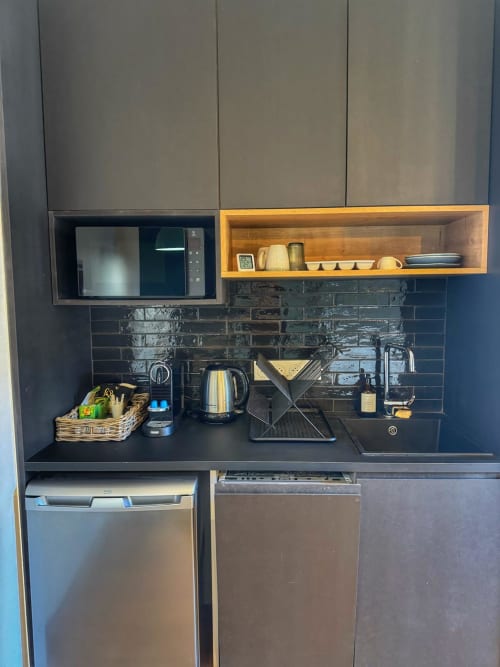 Kitchenette moderne du Studio 1 à O LIT Trouville-sur-Mer avec meubles noirs, électroménagers inox et étagère en bois