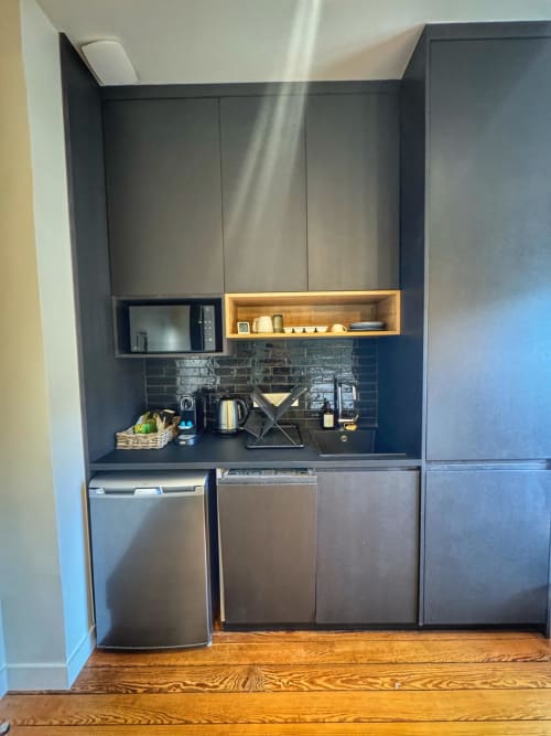 Kitchenette moderne avec armoires sombres, électroménagers en acier inoxydable et étagères en bois au studio O LIT