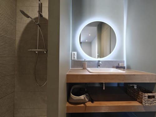 Salle de bain moderne du O LIT Trouville-sur-Mer avec miroir rond illuminé, meuble vasque en bois et pommeau de douche cascade