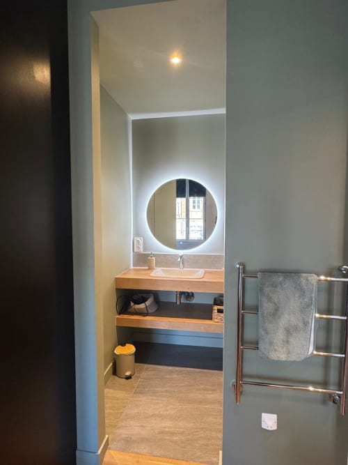 Salle de bain moderne du studio O LIT à Trouville-sur-Mer, avec miroir LED circulaire, meuble vasque en bois et radiateur sèche-serviettes