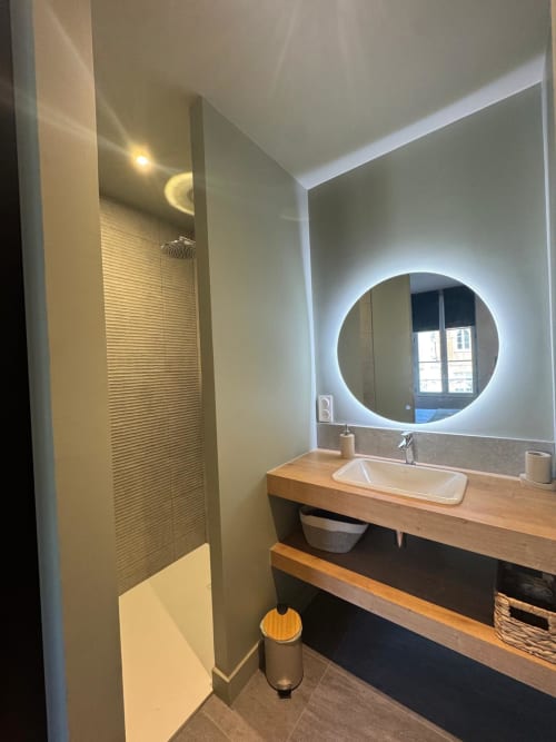 Salle de bain moderne du Studio 2 à O LIT Trouville avec miroir rond illuminé, meuble lavabo en bois et douche à l'italienne