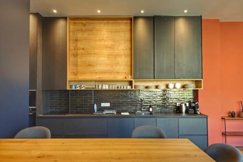 Cuisine loft moderne avec mobilier sombre, étagères en bois, dosseret en carrelage noir et mur d'accent orange à l'hôtel O LIT