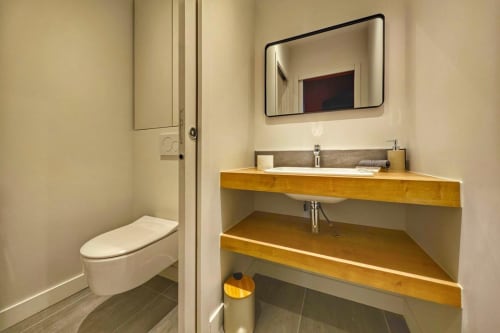 Salle de bain moderne avec toilettes, vasque blanche, meuble en bois et miroir noir arrondi à O LIT Loft à Trouville-sur-Mer