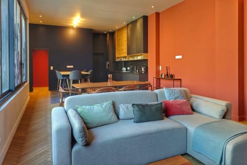 Appartement loft moderne à O LIT à Trouville-sur-Mer avec canapé gris, murs oranges, salle à manger et cuisine ouverte.