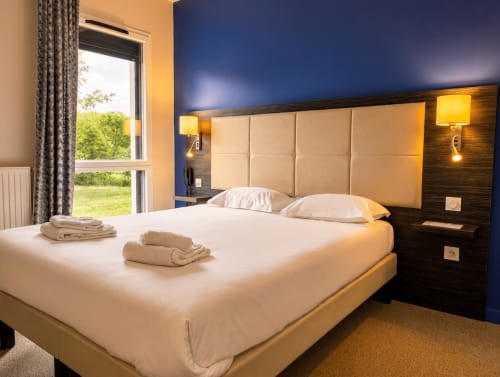 Chambre moderne de l'hôtel La Verriaire avec lit queen-size, mur d'accent bleu et vue sur le jardin à Chanverrie, France