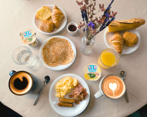 Petit-déjeuner français à l'hôtel La Verriaire avec croissants, crêpes, café, jus d'orange et pâtisseries sur table beige.