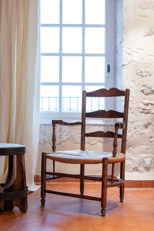 Rustic wooden chair with woven rush seat at Mas Bella Cortis, La Garde-Adhémar, overlooking countryside through tall windows