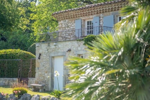 Rustic stone B&B building with blue shutters and balcony at Mas Bella Cortis in La Garde-Adhémar, surrounded by lush greenery