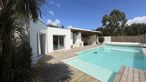 Villa Elara à Mimizan : villa moderne blanche avec piscine turquoise, terrasse en bois et palmiers