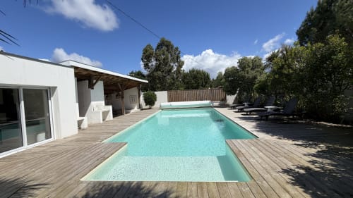 Vue de la piscine de la Villa Elara à Mimizan avec bassin turquoise, terrasse en bois, villa blanche et paysagement luxuriant
