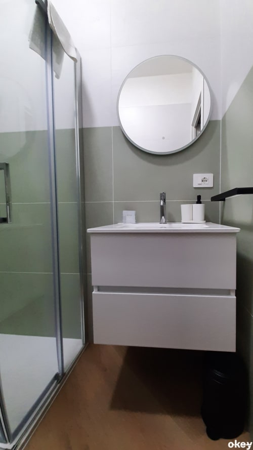 Bagno moderno con vanità bianca, specchio rotondo e piastrelle verdi presso il B&B Bari Centro a Bari, Italia