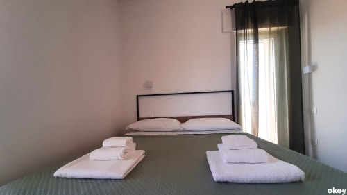 Camera moderna presso B&B Bari Centro con letto matrimoniale, asciugamani bianchi freschi e vista sul giardino attraverso grandi finestre nere