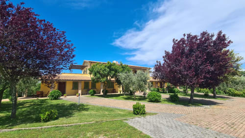 Villa jaune aux jardins luxuriants d'Agriturismo Buriano à Lubriano, Italie, avec ses terrains paysagés et ses allées en brique.