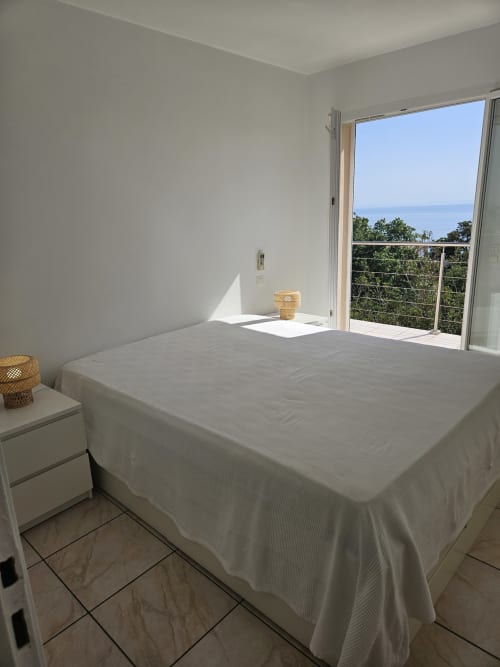 Chambre lumineuse de la Villa Eva gérée par la conciergerie  Corsu Di Core avec vue mer depuis le balcon, lit blanc et équipements modernes à Favone