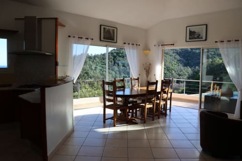 Salle à manger de la Villa Eva avec vue sur les montagnes, cuisine équipée et portes vitrées donnant sur la terrasse géré par la conciergerie Corsu Di Core, Solenzara