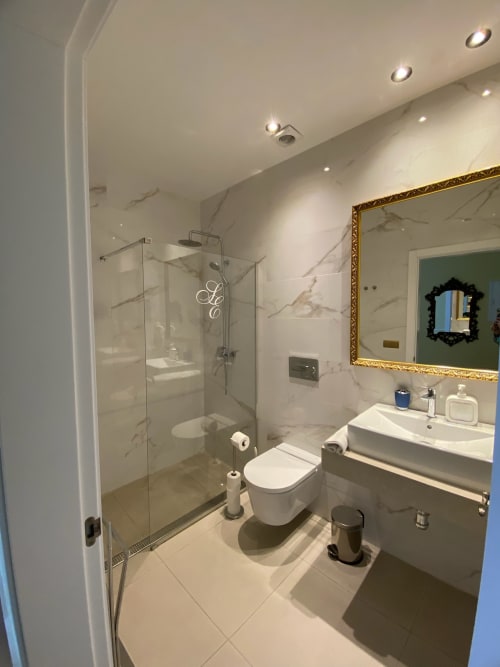 Modern bathroom in Seville hotel suite with marble walls, glass shower enclosure, white sink, and gold-framed mirror