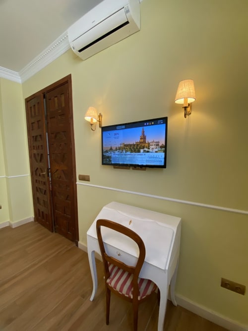 Modern hotel suite in Seville with wall-mounted TV, wooden doors, yellow walls, wall sconces, and wooden flooring