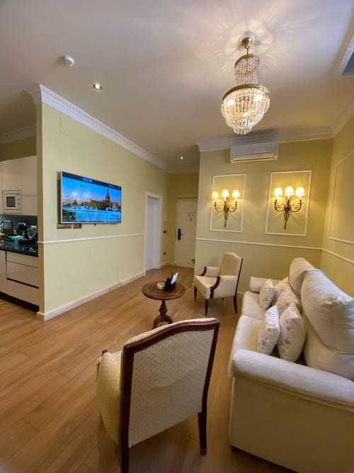 Elegant Seville apartment suite with yellow walls, cream sofa, chandelier, and flat-screen TV displaying city views