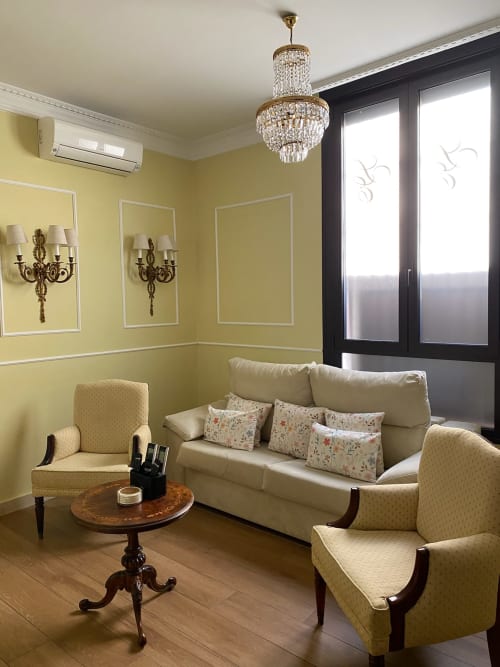 Elegante sala de estar en suite de hotel sevillano con paredes amarillas, lámpara de cristal, sofá color crema y sillones con estampado floral