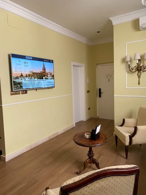 Bright yellow hotel suite in Seville with flat-screen TV, wooden furnishings, and cream upholstered chairs