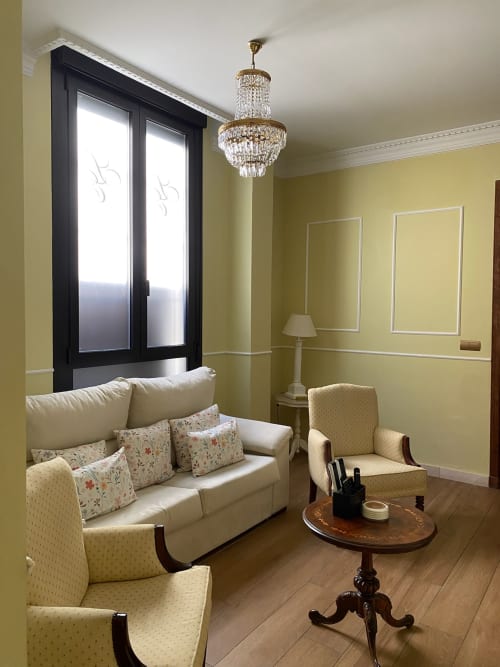 Elegant Seville suite living room with yellow walls, crystal chandelier, cream sofa, and city view windows at Edificio San