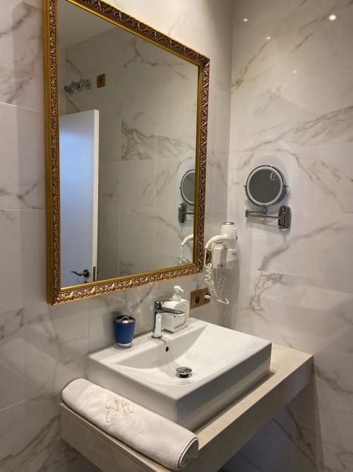 Luxury bathroom in Seville hotel suite with marble walls, gold-framed mirror, white vessel sink, and amenities