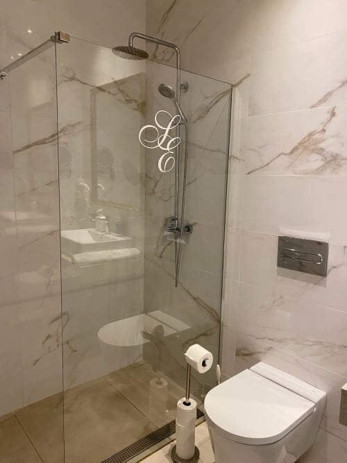 Modern bathroom in Sevilla hotel suite with marble tiles, glass shower enclosure, white toilet, and rainfall showerhead.