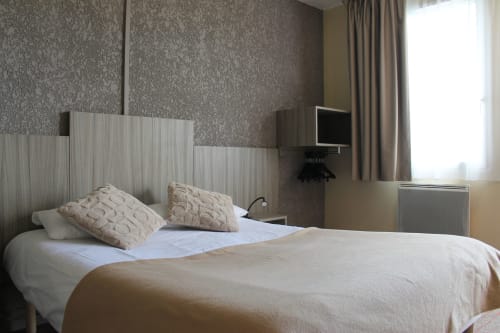 Chambre accessible à Libre Hôtel avec oreillers beiges, literie blanche, téléviseur écran plat et vue sur le jardin par fenêtre à rideaux