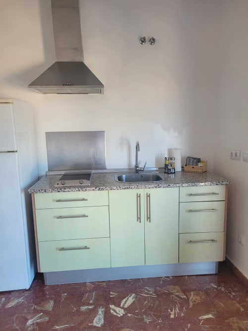 Cocina moderna con gabinetes verde claro, encimera de granito, fregadero, estufa y campana extractora en Apartamento 1 de Apartamentos A
