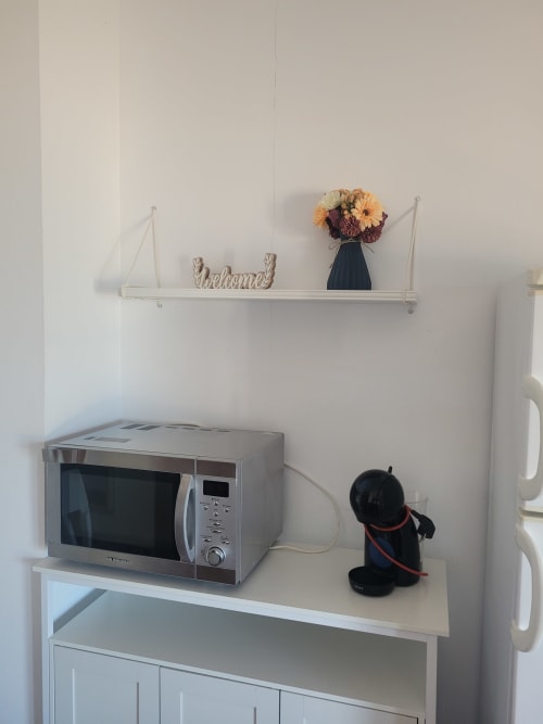 Microondas y hervidor en estantería blanca con letrero de bienvenida y flores en apartamento de Apartamentos A la Orilla del Mar