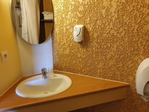 Salle de bains accessible du Libre Hôtel avec lavabo rond, miroir, distributeur de savon et murs en liège texturé à La Vespière, France