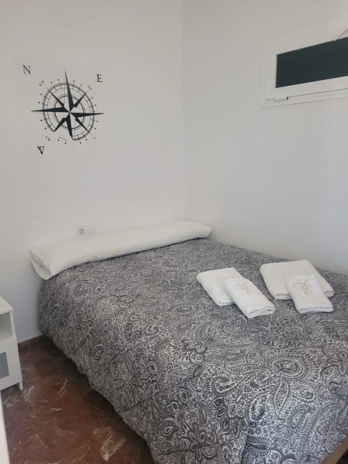 Dormitorio en Apartamentos A la Orilla del Mar en Matalascañas con ropa de cama estampada, almohadas blancas y brújula en la pared