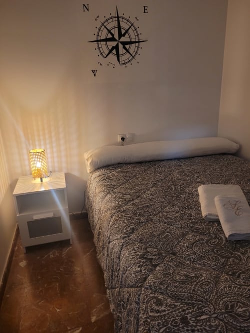 Dormitorio acogedor en Apartamentos A la Orilla del Mar con decoración de brújula, ropa de cama estampada y lámpara de noche.