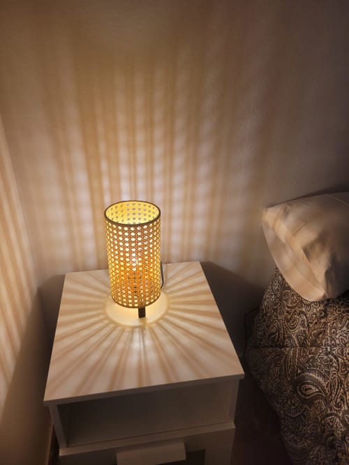 Lámpara de mesa decorativa con pantalla cilíndrica tejida que proyecta patrones geométricos en la pared del dormitorio, Apartamentos A la Orilla