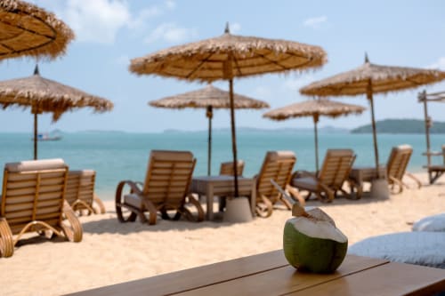 Allestimento spiaggia tropicale al CONDHOTEL VIENNA con ombrelloni in paglia, lettini in legno e bevanda al cocco a Pesaro