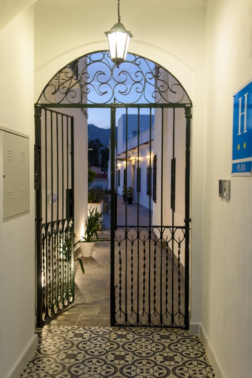 Puerta de hierro forjado ornamentado con arco de transom en la entrada del Hotel Alcazaba Salobreña, conduciendo al patio iluminado al atardecer