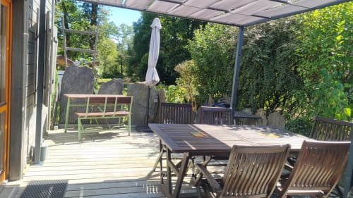 Terrasse ensoleillée du Clos du Tay avec table à manger, chaises, parasol et verdure luxuriante à La Gacilly