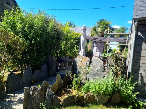 Jardin arrière luxuriant aux Chambres d'hôtes le Clos du Tay à La Gacilly avec éléments en pierre, parasol et pergola