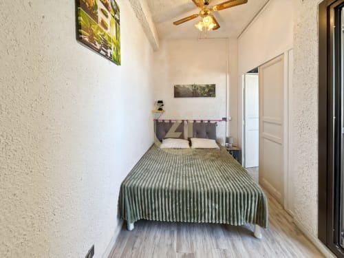 Chambre compacte avec couvre-lit vert rayé, ventilateur de plafond et murs blancs texturés à l'appartement Century 21 de L'Île-Rousse