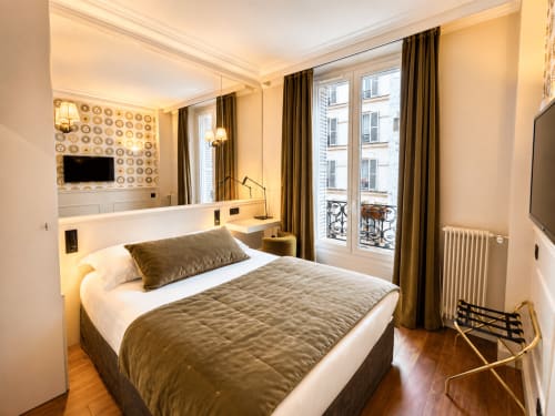 Chambre moderne de l'Hôtel des Bains avec lit queen-size, rideaux dorés, vue sur la ville et éclairage ambiant