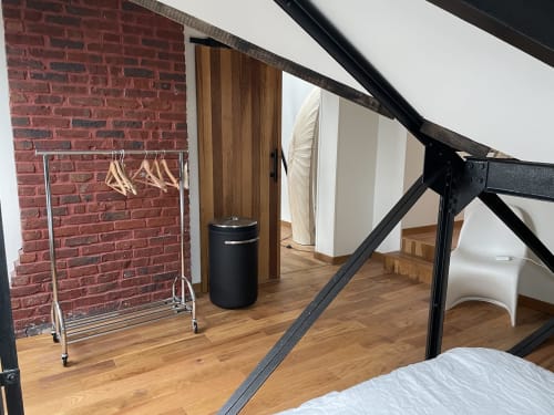 Modern loft bedroom at Villa Sonneville in Roubaix with exposed brick, wooden floors, black metal frame bed and clothing rack