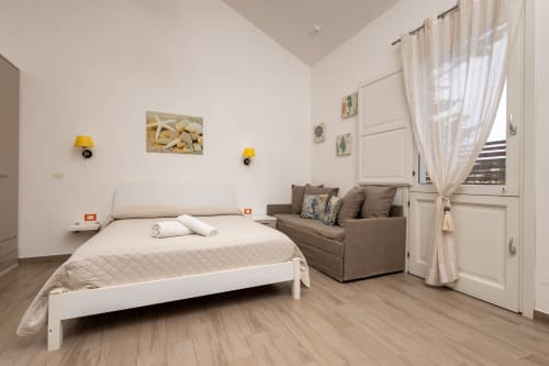 Bright bedroom at Senia del Rais in Favignana with white bed, brown sofa, and ocean view through door