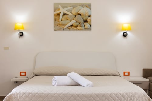 Modern bedroom at Senia del Rais in Favignana with beige bed, rolled towels, starfish wall art, and yellow lamps