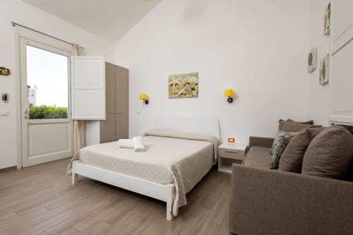 Bright bedroom at Senia del Rais in Favignana with queen bed, sofa, and ocean view through patio door