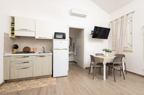 Modern kitchenette and dining area in Cavaluccio Marino room at Senia del Rais, Favignana, with wooden cabinets, white