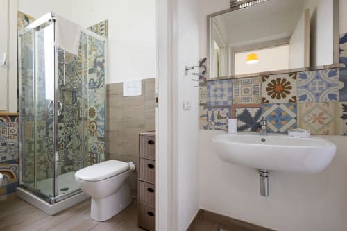 Modern bathroom at Senia del Rais in Favignana with patterned tile backsplash, walk-in shower, toilet, and wall-mounted sink