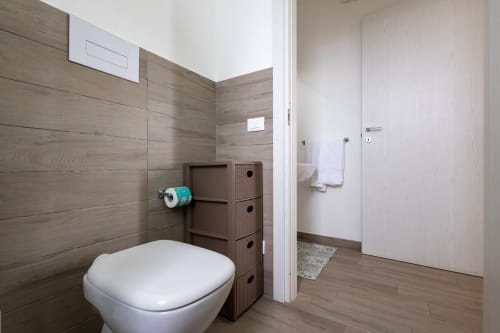 Modern bathroom in Senia del Rais, Favignana with wood-tiled walls, white toilet, and storage unit